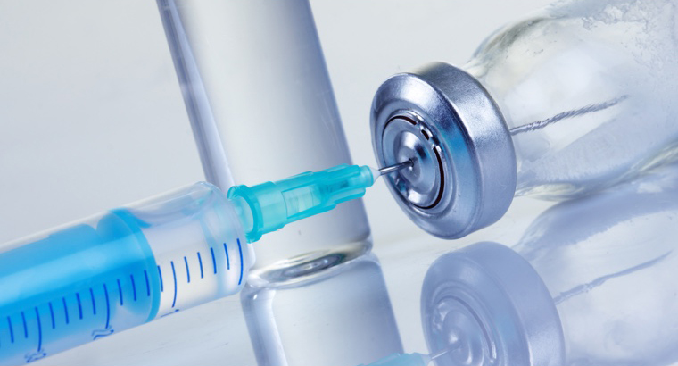 A hypodermic needle inserted into the top of a vial of medication.