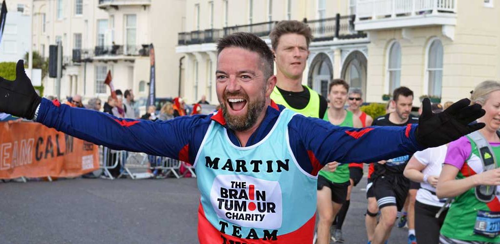 A man running in The Charities vest with his arm out wide and smiling.