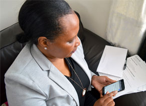 A Black woman in a smart blazer fills in Work Tax Credit forms while using her mobile phone to look up information.