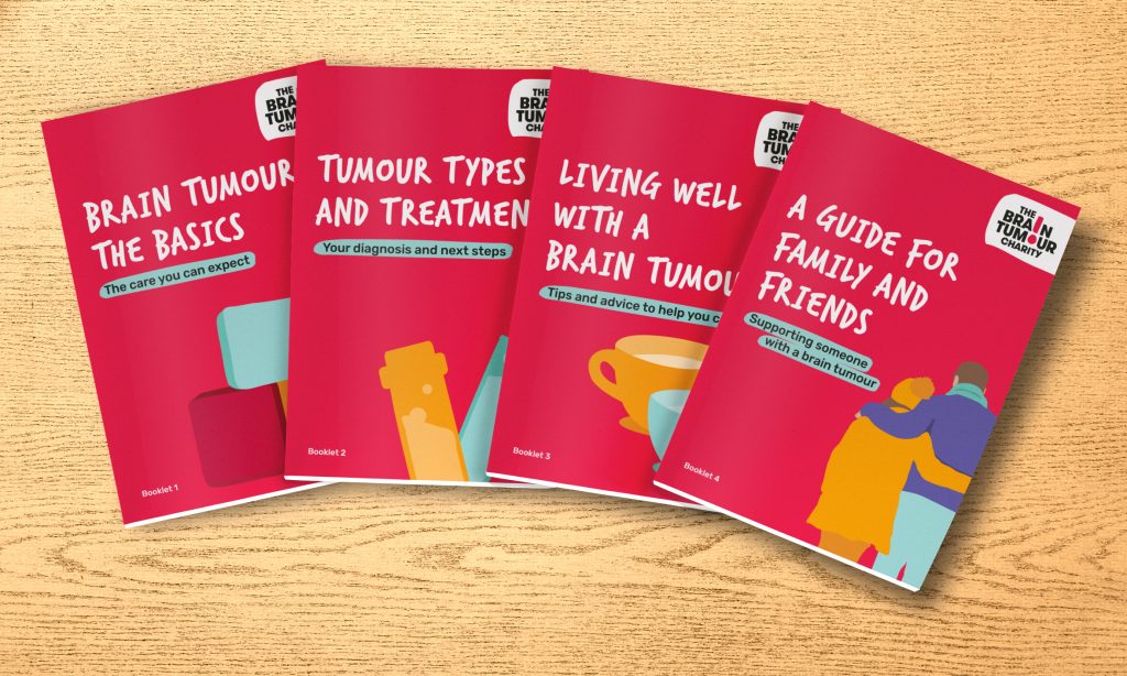 The four booklets that make up our Brain Tumour Information Pack are spread across a wooden desk. They're titled - "Brain Tumours:The Basics", "Tumour types and treatments", "Living well with a brain tumour" and "A guide for family and friends".