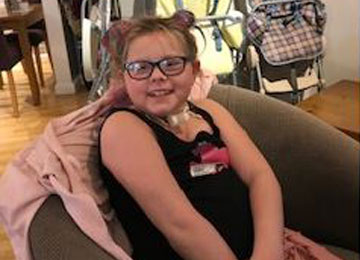 Maisie, a young girl diagnosed with a brain tumour, poses for a photo in an over-sized armchair.