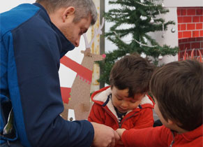 A man plays with his two young children against the backdrop of a Christmas decorations.